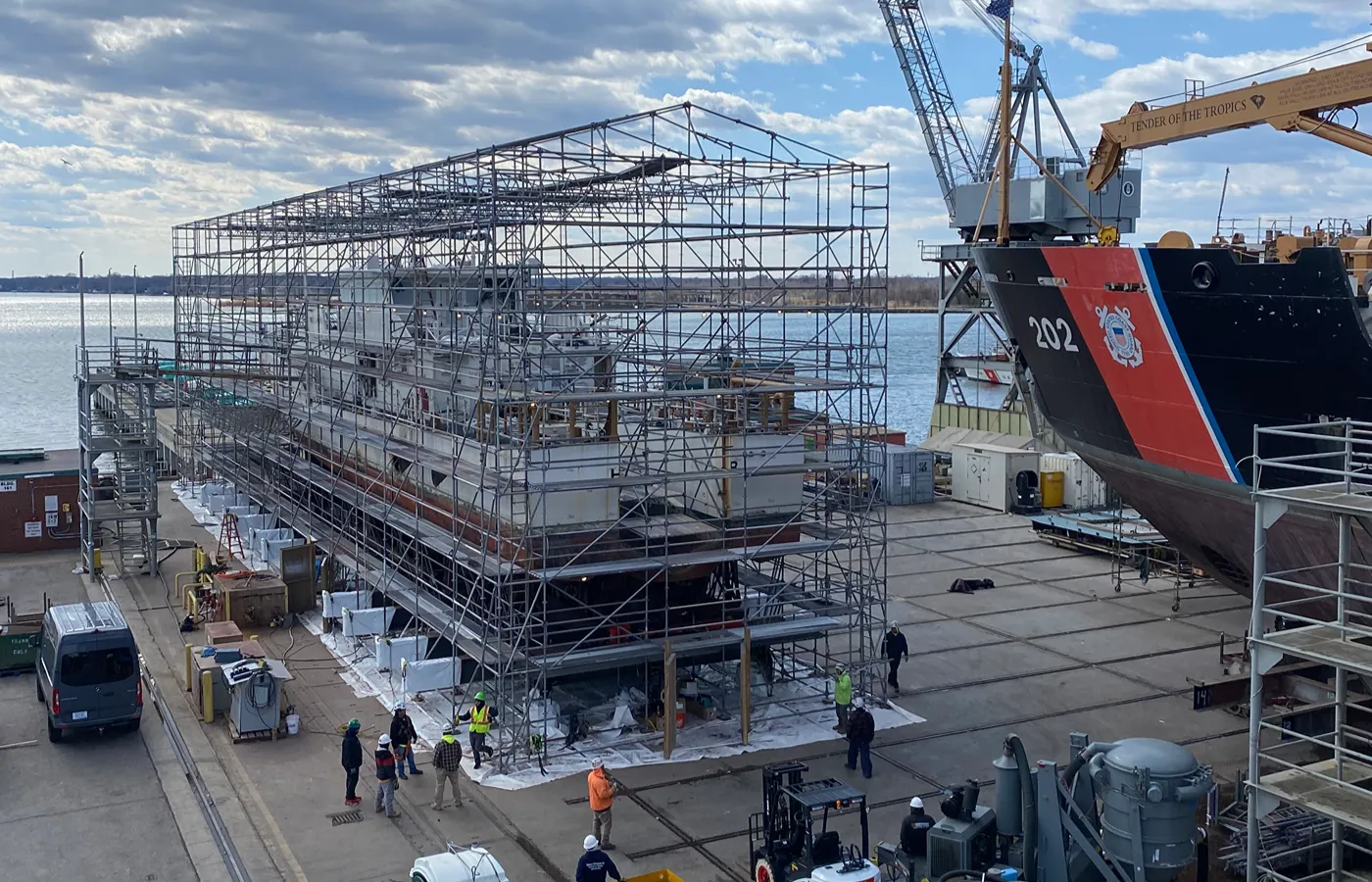 Shipyard vessel enclosed in a full scaffolding structure beside a U.S. Coast Guard cutter