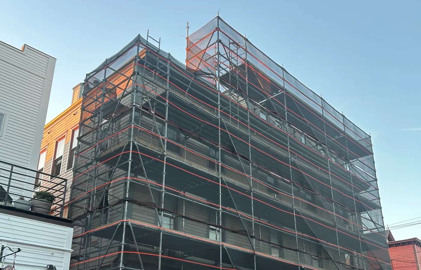 Urban building covered in scaffolding with debris netting and red safety rails